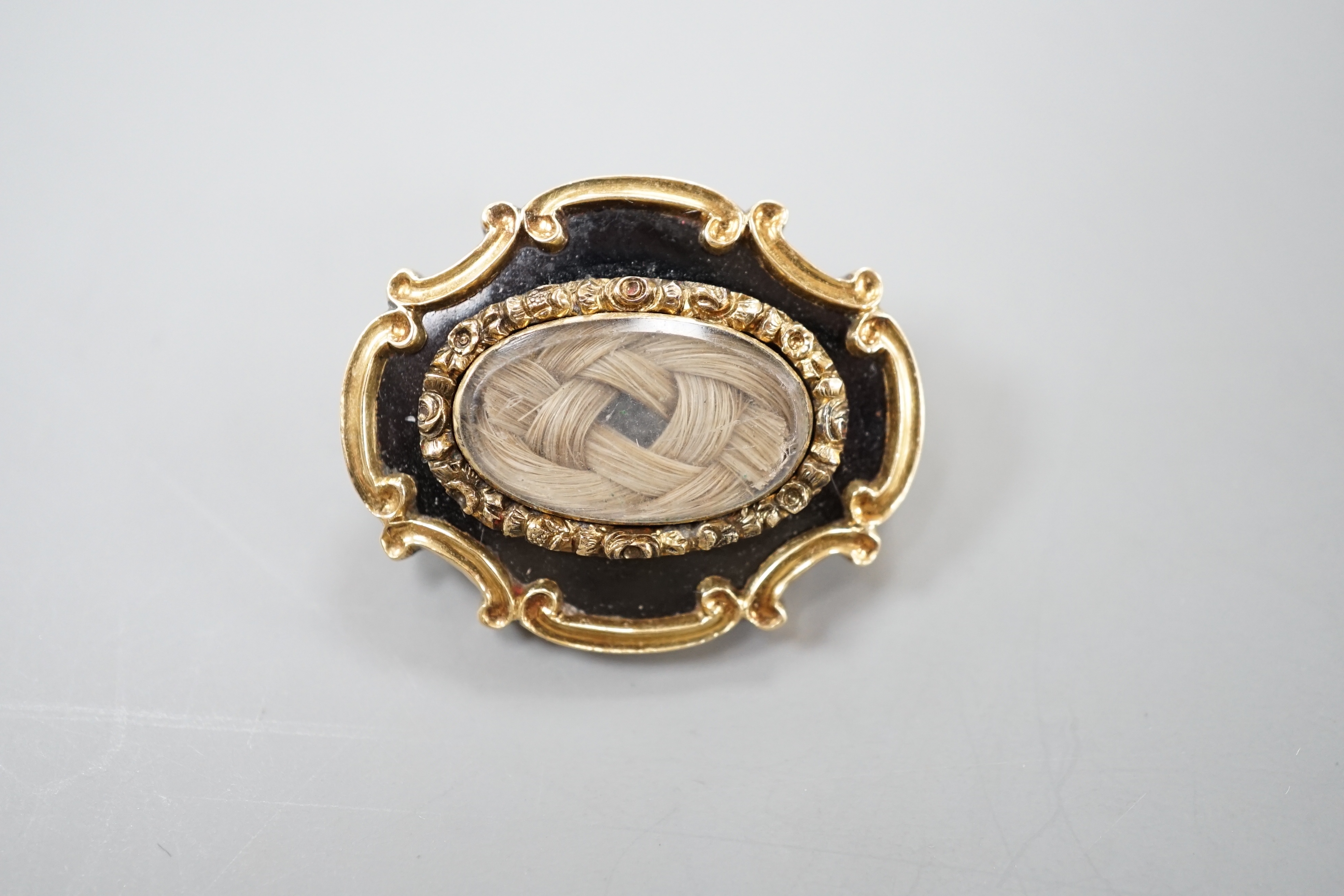 An early Victorian yellow metal, black enamel and plaited hair mourning brooch, inscribed verso, 'Revd. JWH Marshall Obt 23rd March, 1841 at 38', 27mm.